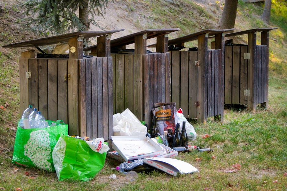 An expansive view of a large landfill site filled with mixed waste materials, predominantly consisting of crumpled plastic bags, paper, discarded packaging, and fragmented cardboard. The waste is spre